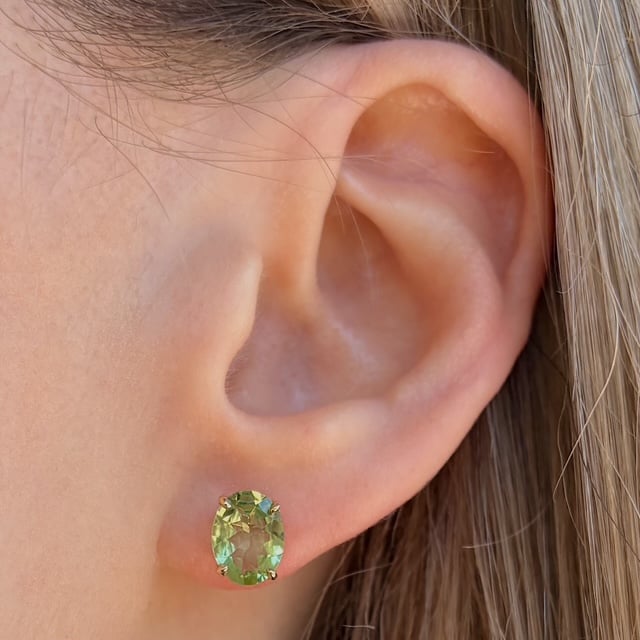 Close-up of a earlobe with a green oval gemstone stud earring in a gold setting