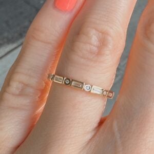 Close-up of a delicate gold ring with alternating rectangular and round stones on a finger.