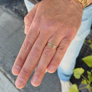 Close-up of a left hand showing a gold wedding band on the ring finger, with a gold watch visible on the wrist.