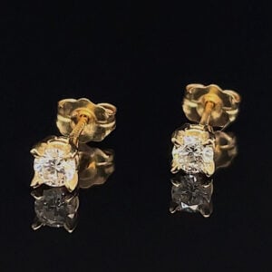 Gold stud earrings with round diamonds on a black reflective surface, close-up view showing prong settings.