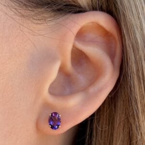 Close-up of a pierced earlobe wearing a purple oval gemstone stud earring.
