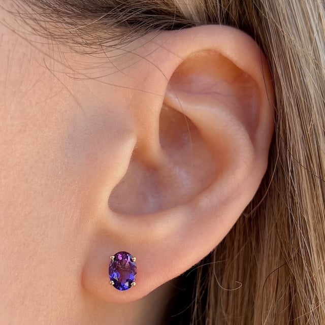 Close-up of a pierced earlobe wearing a purple oval gemstone stud earring.