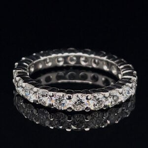 Close-up of a diamond-studded eternity ring (silver metal) on a black background, showing prong-set stones around the band.