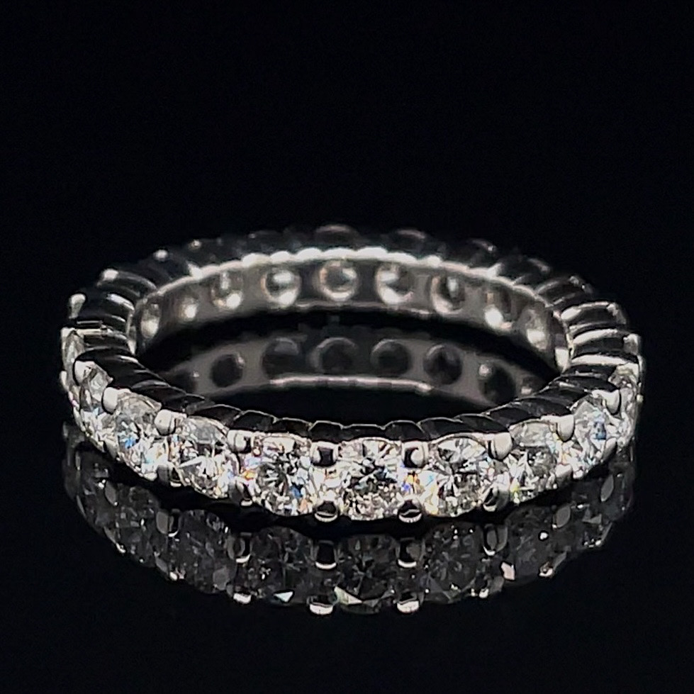 Close-up of a diamond-studded eternity ring (silver metal) on a black background, showing prong-set stones around the band.