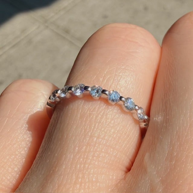 Delicate silver ring with small blue gemstones along a thin band on a finger in sunlight.