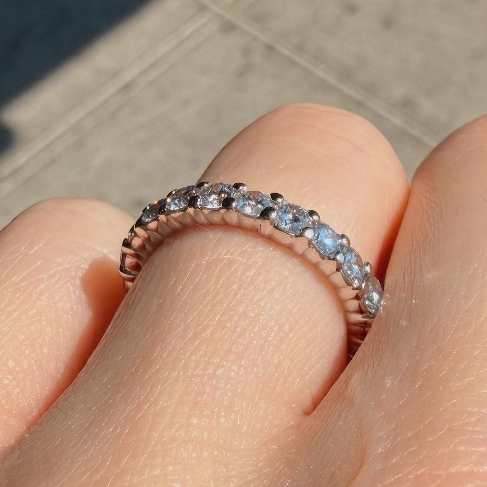 Close-up of a diamond eternity ring on a finger, showing a row of clear stones set in a rose-gold band.