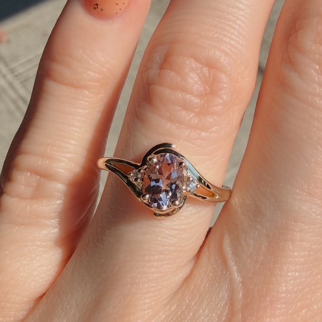 Gold ring with an oval lavender gemstone and small side diamonds, worn on a finger.