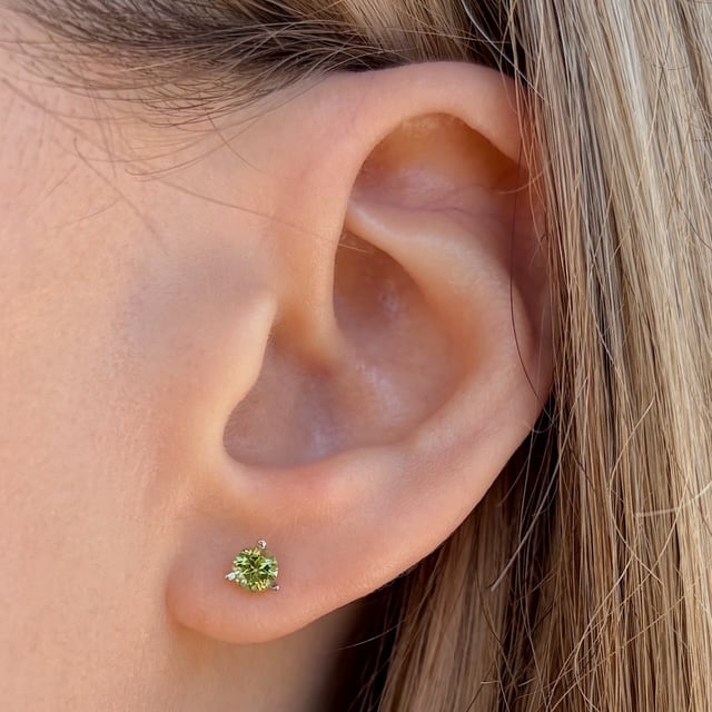 Close-up of an ear with a small green gemstone stud earring worn on the earlobe (peridot).