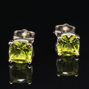 Pair of silver stud earrings featuring cushion-cut lime-yellow gemstones on a dark reflective surface.