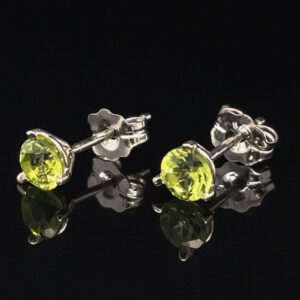 Pair of silver stud earrings, each with a bright lime-yellow peridot gemstone in a prong setting, against a black reflective background.