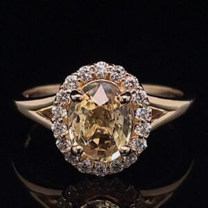 Oval yellow diamond halo ring set in gold, surrounded by a circle of small diamonds on a black background.