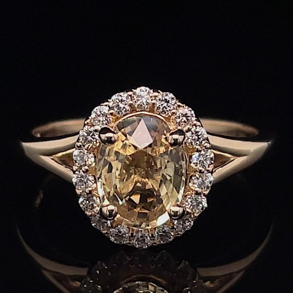 Oval yellow diamond halo ring set in gold, surrounded by a circle of small diamonds on a black background.