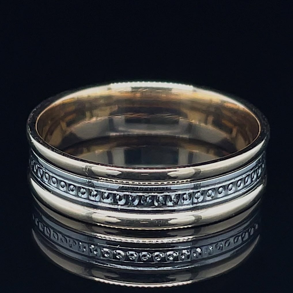 Silver two-band ring with a beaded midsection, photographed on a dark reflective surface
