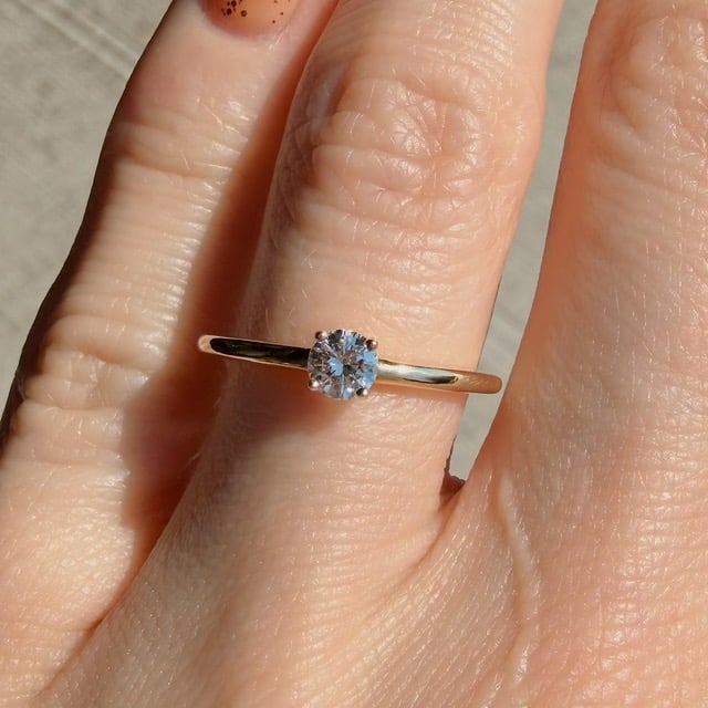 Solitaire diamond ring on a thin gold band worn on a finger, close-up shot in daylight