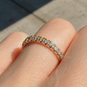 Close-up of a diamond eternity ring with small stones around a rose-gold band on a finger's edge.
