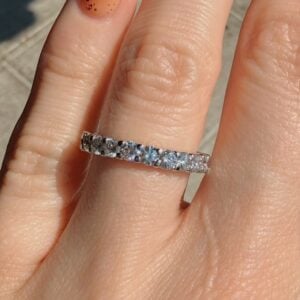 Close-up of a silver eternity ring with round-cut diamonds on a finger, sunlight highlighting the stones
