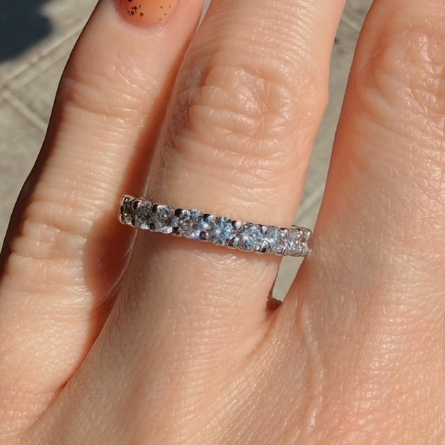 Close-up of a silver eternity ring with round-cut diamonds on a finger, sunlight highlighting the stones