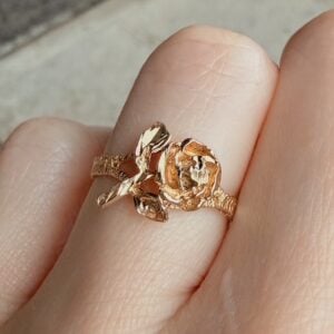 Gold ring with a rose-shaped centerpiece worn on a finger on close-up view.