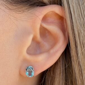 Close-up of a woman's left ear wearing a blue oval gemstone stud earring in a silver setting