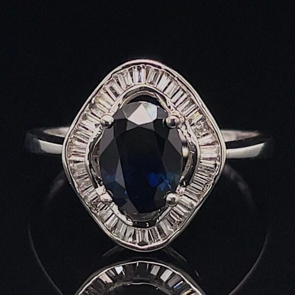 Silver ring with a dark blue oval cushion-cut center stone, surrounded by a halo of baguette diamonds on a black background.