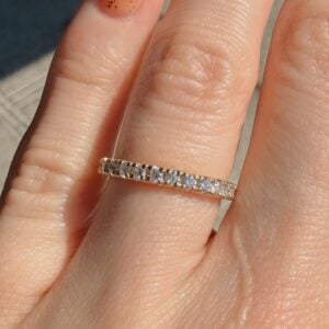 Close-up of a thin gold band ring with small diamonds on a finger, pavé-set stones catching the light.