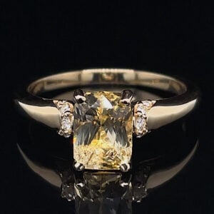 Engagement ring with a large rectangular yellow gemstone and diamond side stones on a gold band.