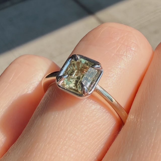 Silver ring with a square cushion-cut light green gemstone on a finger in sunlight.