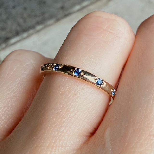 Close-up of a gold ring adorned with small blue sapphires on a finger