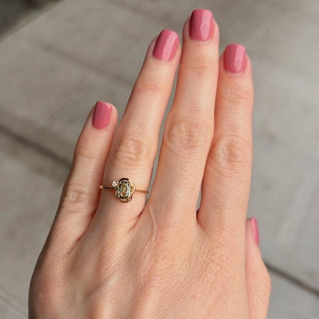 Close-up of a hand with pink-painted nails wearing a gold ring with a small gemstone on the ring finger.