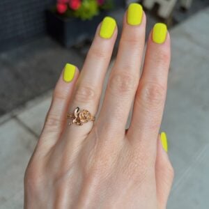 Close-up of a hand with neon yellow nail polish on all fingers, wearing a delicate gold ring on the ring finger.