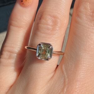 Rose gold ring with a square-cut pale green gemstone held by four prongs on a finger.