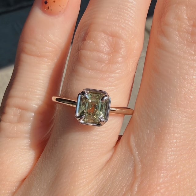 Rose gold ring with a square-cut pale green gemstone held by four prongs on a finger.