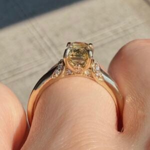 Rose gold engagement ring with a large oval yellow center stone and diamond-accent shoulders on a finger.