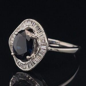 Oval black/dark blue gemstone ring with a halo of rectangular clear stones set in white metal.