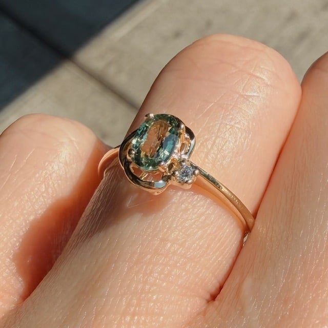 Gold ring with an oval green gemstone and a small accompanying diamond on a finger.
