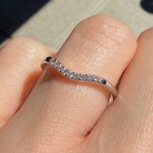 A silver ring with a row of small diamonds worn on a finger outdoors in sunlight.