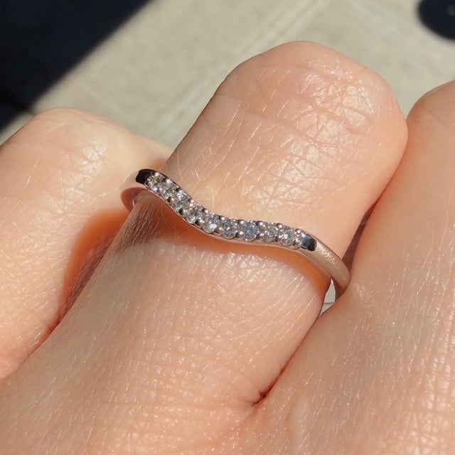 A silver ring with a row of small diamonds worn on a finger outdoors in sunlight.