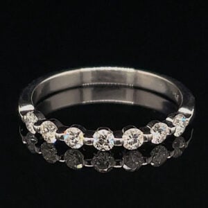 Silver ring with alternating round diamonds set along the top half of the band against a black background.