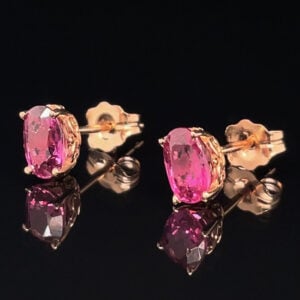 Pink oval-cut gemstone stud earrings with gold prong settings on a reflective black surface.