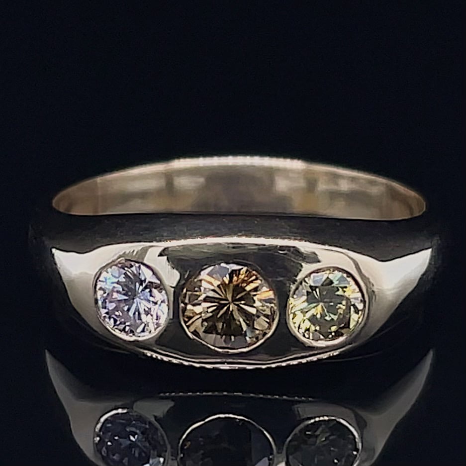 Silver ring with three evenly spaced round-cut gems—blue left, champagne center, pale yellow right—on a dark background.