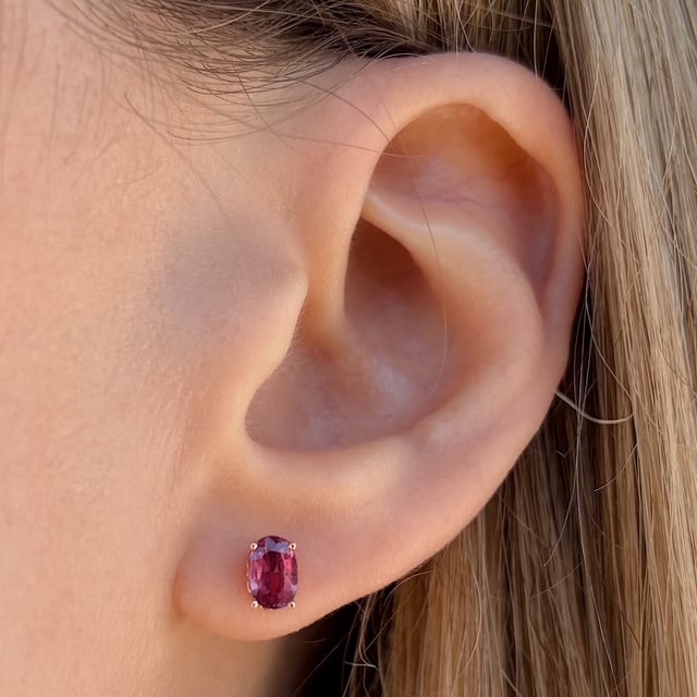 Close-up of an ear with a pink-purple oval gemstone stud earring secured by prongs.