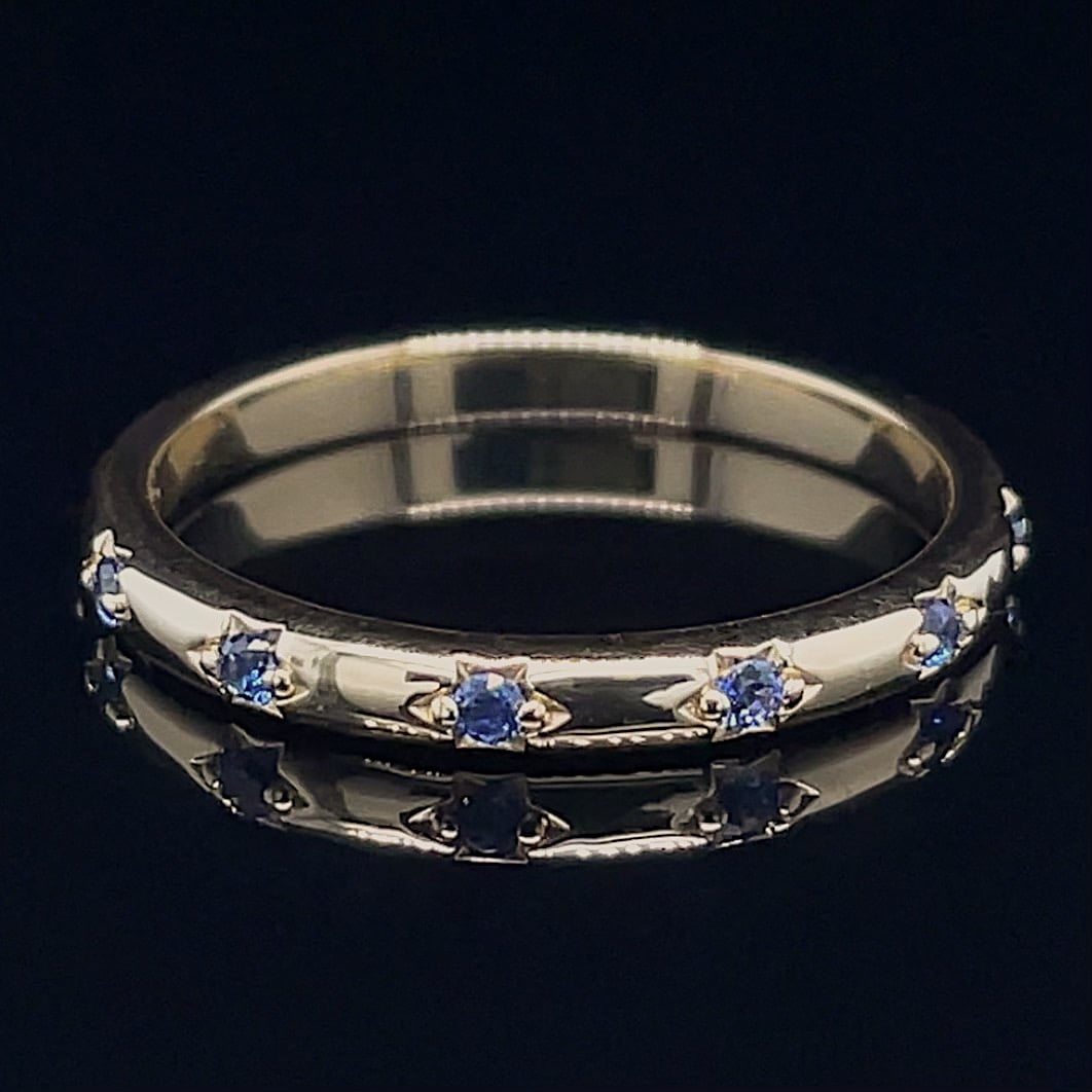 Silver ring with small blue gemstones set evenly around the band.