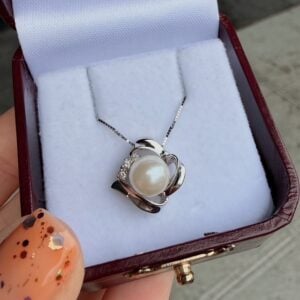 Pearl pendant necklace in a silver, floral-style setting inside a burgundy jewelry box.