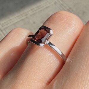 Close-up of a silver ring with a pink rectangular gemstone on a finger