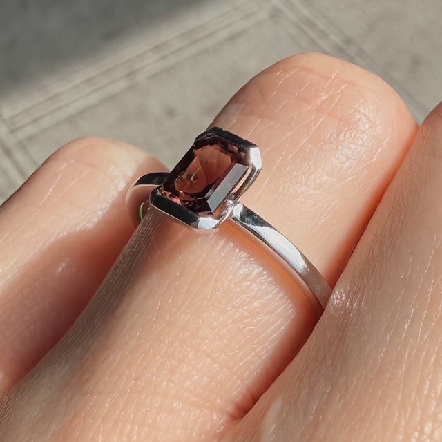 Close-up of a silver ring with a pink rectangular gemstone on a finger