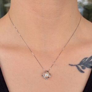 Delicate silver chain with a pearl pendant resting at the base of the neck, tattoo visible on the shoulder area.