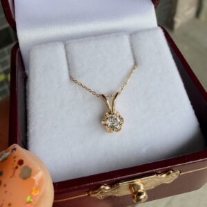 Gold delicate chain necklace with a round diamond pendant in a flower-shaped setting inside a white padded jewelry box.
