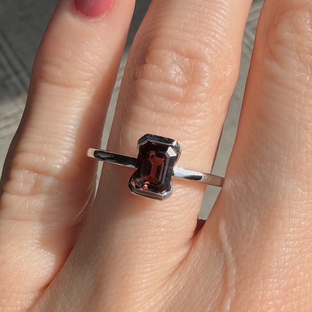 Silver ring with a rectangular emerald-cut dark red gemstone on a finger