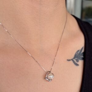 Silver chain necklace with a small pearl pendant resting near the collarbone, with a bird tattoo visible on the shoulder area.