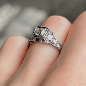 Close-up of a silver Art Deco ring with a central square diamond and smaller square-cut stones on the band, on a finger.